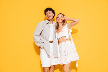 Happy beautiful romantic teenage couple. Smiling handsome caucasian man and young woman in summer clothes posing in studio, hugging sharing positive emotions, cheerful and happy. Isolated on yellow