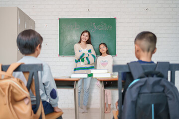 young asian female teacher introduces new schoolgirl to children in elementary school classroom