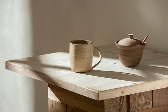 An elegant minimalist concept featuring modern ceramic mugs and cups on a neutral beige wooden table background. Minimalist design.