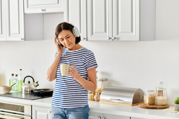 A mature woman in cozy homewear talking on a cell phone in a kitchen.