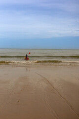 A man in canoe next to an empty sandy beach at low tide on a sunny day.