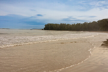 A tranquil view of on a sandy beach in the morning with clouds and blue horizon. Gentle waves on the sea at low tide. Phuket, Nai Yang Beach