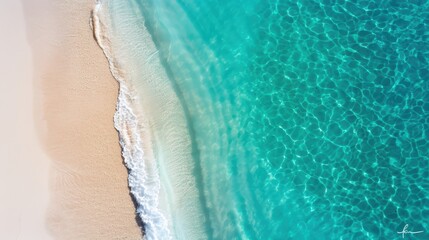 A breathtaking aerial view of aqua blue ocean waves gently lapping against a pristine sandy beach, displaying the striking natural beauty and clarity of the coastal region.