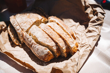 Captured in natural lighting, a rustic, artisanal sourdough bread is freshly baked and sliced on brown paper, appealingly presented as a savory snack or breakfast option