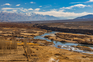 Indus river flowing through dry winter grass with snow-clad mountains around in Ladakh 