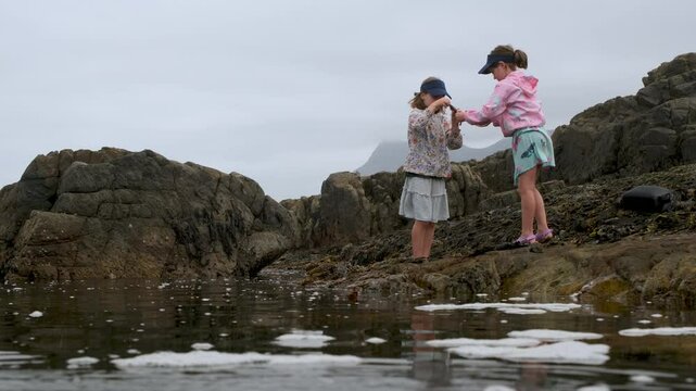 Low angle over rockpool of two avid fishermen girls removing hook from klipfish