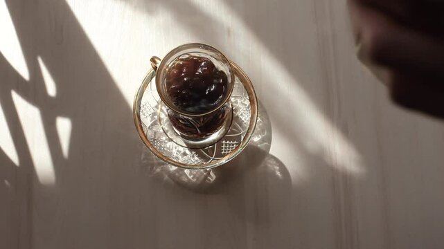 Morning coffee is poured into a glass on a white table. A glass of coffee in the sun.