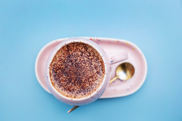 Beautiful mocha drink in speckled pink cup on matching saucer, with golden antique spoon on blue 