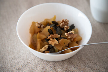 Bowl of baked apple with cinnamon, walnuts and pumpkin seeds, healthy breakfast on a beige tablecloth.