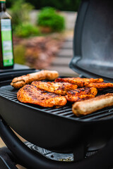 Delicious Chicken Steaks and Sausages Getting Grilled on a Hot Black Grill Grate off a Small Electrical Garden Grill