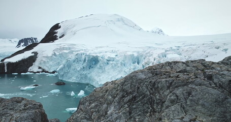 Antarctica coastline bay with rocks and glacier towering over polar ocean water. Snow covered mountains, calving ice floes. Amazing winter landscape. Travel Antarctica. Explore South Pole wild nature