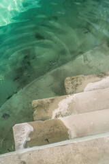 Concrete steps leading into a clear, green-hued body of water, capturing the serene and refreshing essence of a waterfront location