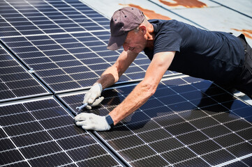 Worker building photovoltaic solar panel system on rooftop of house. Close up of man engineer...