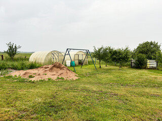 A summer cottage with two greenhouses, apple trees, a sand pile, and a metal swing frame