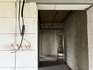 A bike is hanging on the wall, and in the distance, through the opening, you can see a small stepladder at the construction site of a house made of aerated concrete