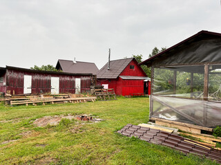 A view of the red bathhouse, a small building with three doors and a gazebo, on a cloudy day at the cottage