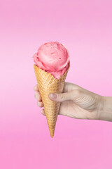 Woman's hand holding waffle cone with strawberry ice cream on pink background food vertical photo