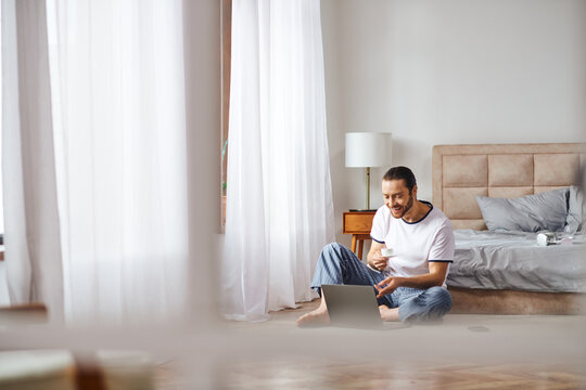 A man immerses himself in online tasks while seated on the floor, blending tranquility with technology.