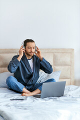 A man is seated on a bed, engrossed in music.