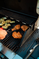 Person Grilling Steaks and Vegetables on a Big Home Gas Grill with Hot Flames During Summer Season on a Sunny Day