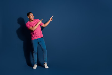 Photo of young guy wearing pink t shirt and denim jeans directing fingers empty space ebay store isolated over dark blue color background