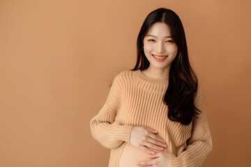 Obraz premium Beautiful Asian Pregnancy happiness woman smile in knit shirt touch belly waiting for unborn baby on beige isolated background. Mom holding tummy. Journey to motherhood.