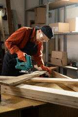 professional female carpenter using wood polishing machine grinding sanding wooden board in her...