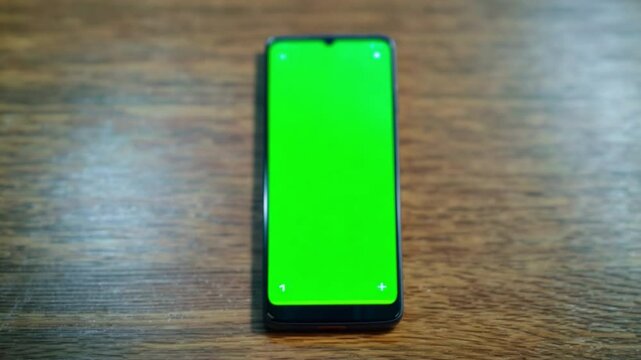 A green phone is on a wooden table. The phone is turned off and has a green screen