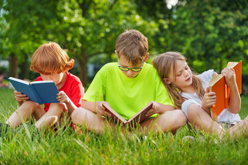 Cute children reading colorful books together outside in the park.