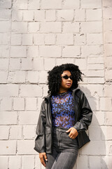 Obraz premium A stylish woman in casual clothes stands by a textured brick wall.