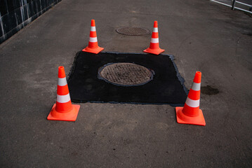 Repair of asphalt on the sidewalk around the sewer manhole fenced with warning orange cones