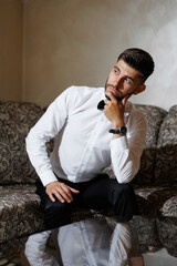 Obraz premium A man in a white shirt and black pants is sitting on a couch, looking at the camera
