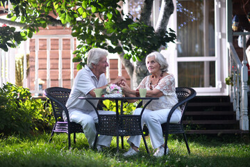 Elderly couple sitting at the table in the summer at the country house