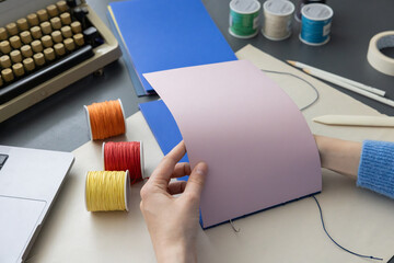 High-quality image of a person binding a book using traditional coptic stitch technique. DIY bookbinding, handcrafting, artisan book, handmade, coptic stitch, binding tools, creative, detailed process