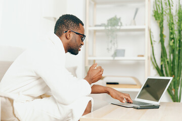 Smiling African American Man Typing on Laptop in his Modern Home Office, Enjoying a Relaxing...