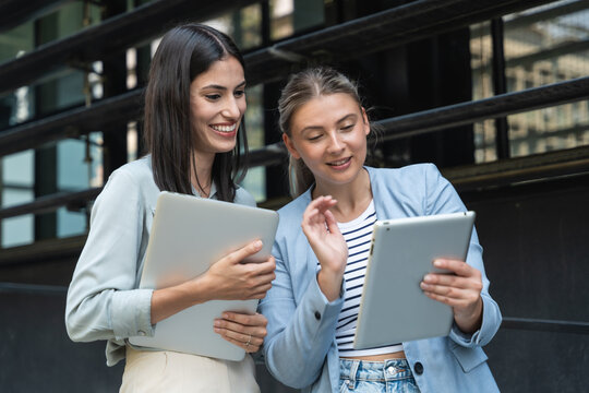Two business women out of office building with laptop and digital tablet. Technology used in modern business life. Sustainable energy experts, developers and design professionals working together.