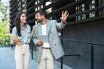 Business man and woman out of office building with laptop and digital tablet. Technology used in modern business life. Sustainable energy experts developers and design professionals working together.