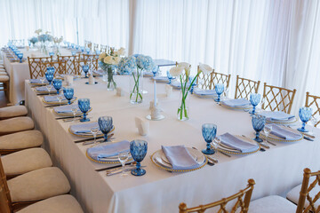 A long table with blue glasses and white table cloth. The table is set for a formal dinner