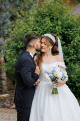 A bride and groom are kissing each other's cheeks. The bride is holding a bouquet of flowers
