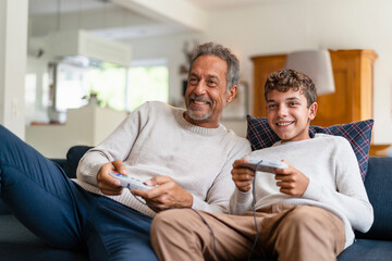 Happy grandfather and grandson playing video game and sitting on sofa at home