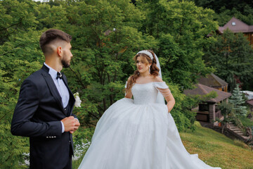 A man and a woman are standing in a lush green field, with the woman wearing a white dress. The scene is romantic and picturesque, with the couple looking into each other's eyes