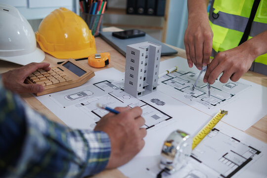 A team of engineers and architects discuss house plan design and estimate construction prices to suit the construction budget. Checking blueprints and documents with a team of engineers and architects - Powered by Adobe