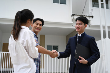 A couple shakes hands with their real estate agent, sharing a happy moment as they finalize the purchase of their new home