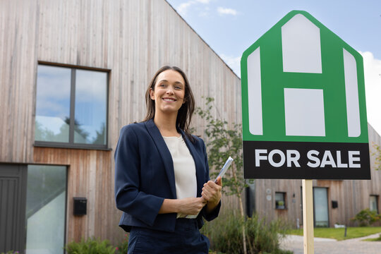 Happy real estate agent standing with a for sale sign for a eco home