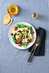 Mediterranean salad with mozzarella, olives, basil and grilled vegetables on a blue striped linen tablecloth