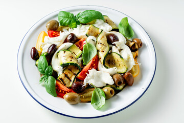 Mediterranean salad with mozzarella, olives, basil and grilled vegetables on white