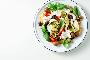 Mediterranean salad with mozzarella, olives, basil and grilled vegetables on white