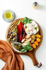 Board with ITALIAN summer foods and grilled vegetables: mozzarella braid, cherry tomatoes, grilled eggplant and zucchini, olives and capers