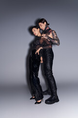 A young tattooed couple posing gracefully in a studio against a grey background.