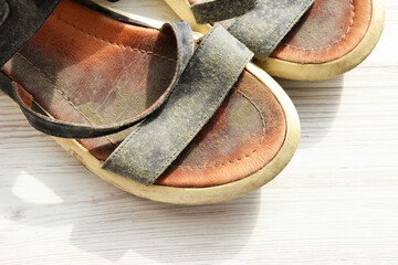 Prevent and remove mould from leather shoes close-up. Summer shoes with abundant mould on a light wood background, top view, with space for text. Pair of summer worn sandals with mold on the surface